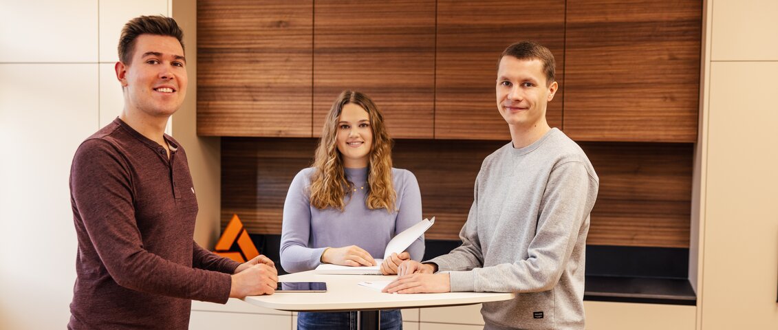 Meeting an einem Stehtisch mit drei Personen mit Blick in die Kamera