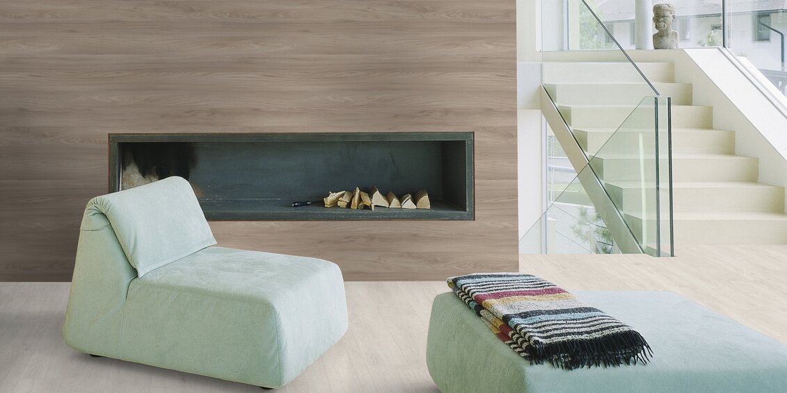 Modernes Wohnzimmer mit eingebautem Kamin, minimalistischen Lounge-Möbeln in Pastellgrün, Holzverkleidung und offener Treppe mit Glasgeländer.
