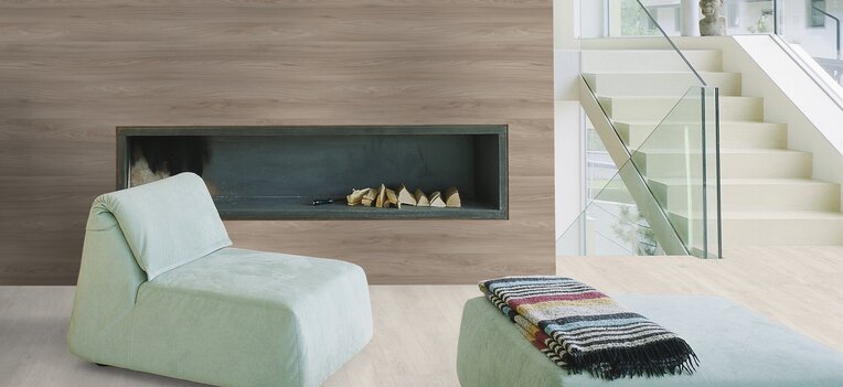 Modernes Wohnzimmer mit eingebautem Kamin, minimalistischen Lounge-Möbeln in Pastellgrün, Holzverkleidung und offener Treppe mit Glasgeländer.