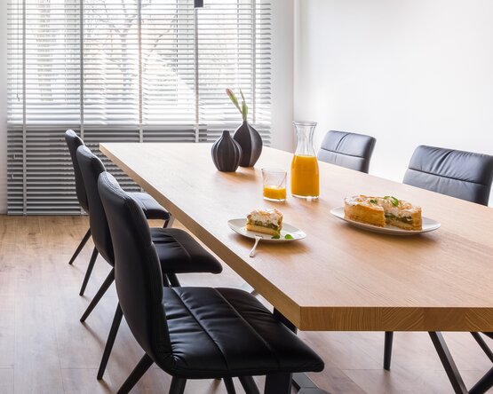 Moderner Essbereich mit Massivholztisch, schwarzen Stühlen und Hängelampen. Auf dem Tisch stehen Kuchen und Saft.