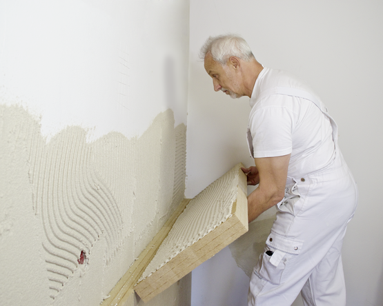 Handwerker bringt Dämmplatte an einer mit Kleber bestrichenen Wand an. | © STEICO