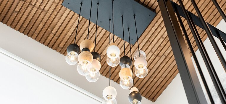 Innenraum mit moderner Holzdecke aus Lunawood Triple, schwarzer Hängeleuchte und schwarzem Geländer.  | © Lunawood