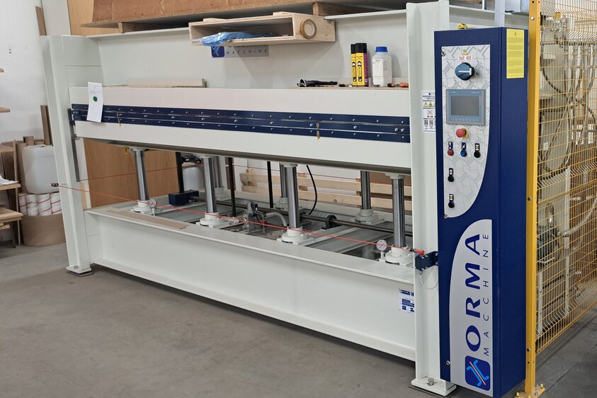 Vlieskaschierung von Holzfurnieren in der industriellen Verarbeitung Eine große Furnier-Vlieskaschierungsmaschine steht in einer Werkstatt und ist gerade am Arbeitsvorgang.