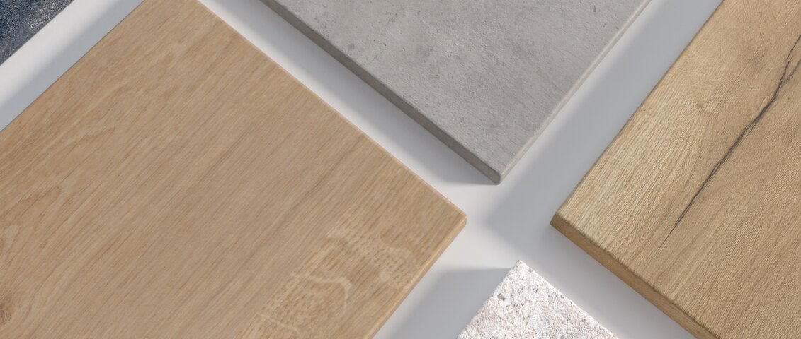 Mehrere schmale Laminatplatten mit unterschiedlichen Dekoren – darunter Holz-, Beton- und Steinoptik – liegen nebeneinander auf einer Fläche. Die Platten wirken wie Musterstücke zur Präsentation verschiedener Oberflächenvarianten für Arbeitsplatten oder Möbelteile.