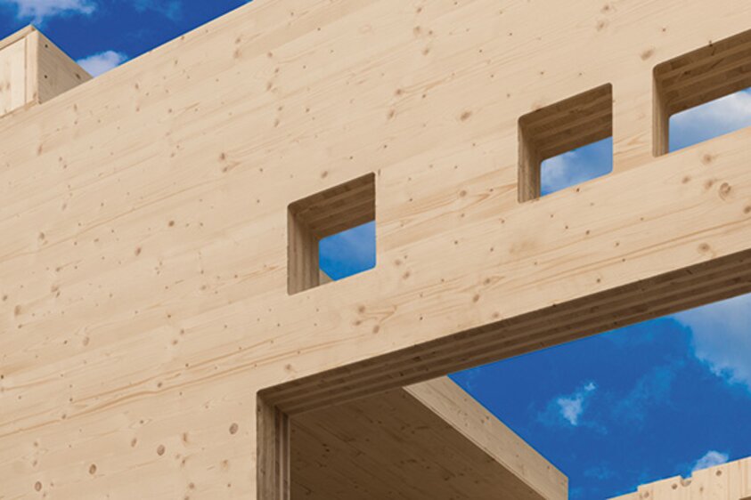 Großformatige Brettsperrholzplatten sind bereits als tragende Bauelemente in einer Holzkonstruktion verbaut. Die Szene zeigt einen modernen Holzbau mit sichtbaren Wand- und Deckenelementen aus Brettsperrholz, die für Stabilität und natürliche Optik sorgen.