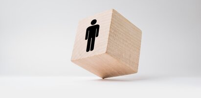 Ein kleiner Holzwürfel mit einem Person-Symbol steht auf einem Eck