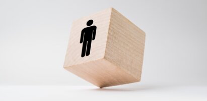 Ein kleiner Holzwürfel mit einem Person-Symbol steht auf einem Eck