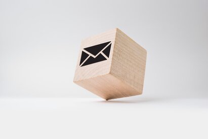 Ein kleiner Holzwürfel mit einem Brief-Symbol steht auf einem Eck