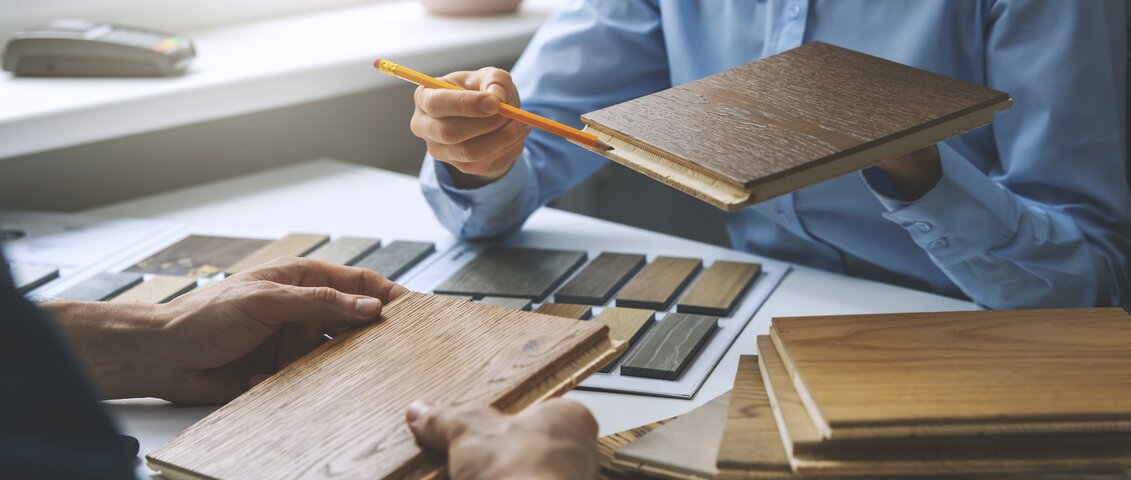 Ein Fachberater spricht mit einem Kunden. Der Berater zeigt auf ein Produkt, während der Kunde aufmerksam zuhört. Die Szene vermittelt eine persönliche und kompetente Beratung rund um Materialien für Bau- oder Ausbauprojekte.