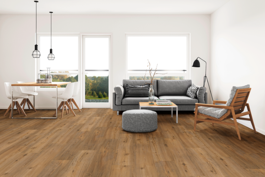 Vinylboden in Holzoptik aus der Eurowood-Kollektion Innenaufnahme eines modernen Wohnzimmers mit einem Vinylboden in realistischer Holzoptik aus der Eurowood-Kollektion. Der Boden hat eine warme, natürliche Maserung und verleiht dem Raum eine gemütliche Atmosphäre. Im Raum befinden sich ein Sofa, ein Couchtisch und stilvolle Dekoelemente, die das wohnliche Ambiente unterstreichen.