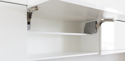 Das Bild zeigt einen geöffneten Küchenschrank mit einem weißen Regalbrett. Sichtbare Scharniere befinden sich an den Seiten. Das Design ist modern und schlicht.