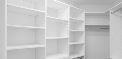 Das Bild zeigt einen weißen, leeren Kleiderschrank mit mehreren offenen Regalfächern und einer Kleiderstange in der Mitte. Keine Gegenstände oder Kleidung sind vorhanden.