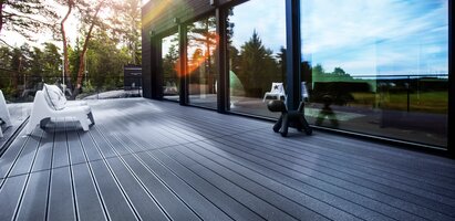 Haus im Wald mit großen Fensterscheiben und mit einer grauen WPC-Terrasse