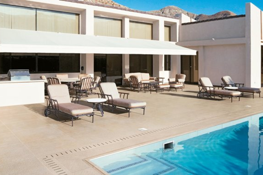 Moderne Poolterrasse mit großformatigen Feinsteinzeugplatten Außenaufnahme einer eleganten Terrasse mit großformatigen Feinsteinzeugplatten in Natursteinoptik, verlegt rund um einen modernen Pool. Die Platten sind in hellen Grau- bzw. Brauntönen gehalten und schaffen eine klare, hochwertige Optik. Im Hintergrund ist eine stilvolle Villa mit großen Glasfronten zu sehen. Die Szene vermittelt mediterranes Flair, modernes Design und exklusives Outdoor-Wohnen.