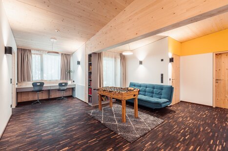 Wohnzimmer mit Holzdecke, Holztüren und Holztischkicker, kombiniert mit modernen Möbeln und Arbeitsplätzen. | © LibertydotHome GmbH