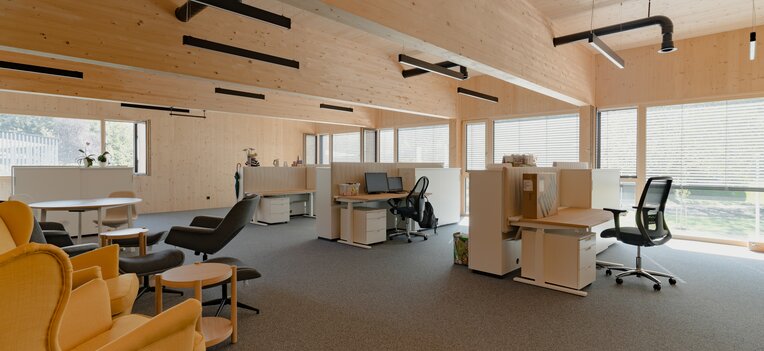 Modernes Büro mit Wänden, Decke und Trägern aus Holz, viel Tageslicht und gemütlicher Sitzecke. | © LibertydotHome GmbH
