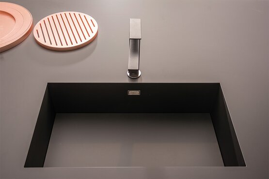 Moderne Spüle in Arbeitsplatte integriert Schwarze Spüle mit eckiger Armatur in glatter Arbeitsplatte, daneben runde pinke Accessoires