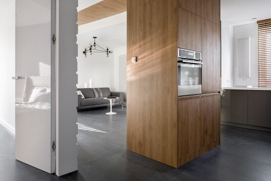 Moderner Wohnraum mit Küche und Wohnzimmer Heller, offener Wohnraum mit moderner Küche, grauem Sofa, weißen Tisch und großen Fenstern mit Holzjalousien.