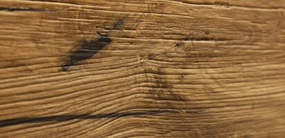 Nahaufnahme einer Holzfläche mit sichtbarer Maserung und dunklen Verfärbungen oder Gebrauchsspuren.