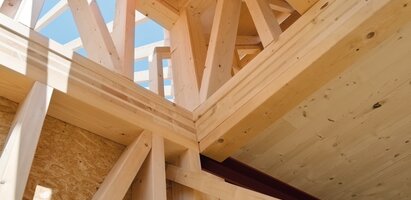 Nahaufnahme eines Holzrahmens mit sichtbaren Balken und Trägern; durch die offenen Stellen ist der Himmel zu sehen.