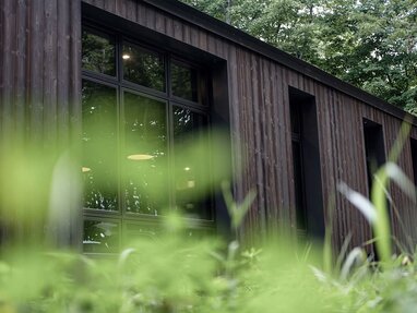 Fassade aus Thermo-Fichte mit vertikalen Holzpaneelen und großen Fenstern, umgeben von grüner Landschaft. | © Will Johnson