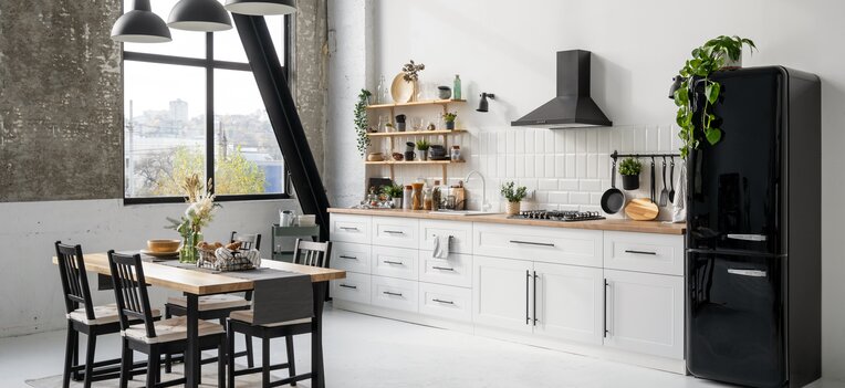 Moderne Küche mit weißen Möbelfronten, Holzarbeitsplatte, schwarzer Dunstabzugshaube und stilvollen Accessoires.