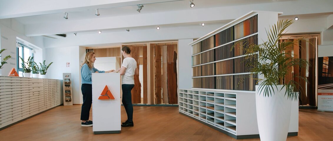 Ein moderner Schauraum mit stilvoller Einrichtung, in dem eine Beratungssituation stattfindet. Der Raum ist hell und einladend gestaltet, mit Mustern und Materialien zur Auswahl. Das Bild vermittelt professionelle Kundenberatung und individuelle Verkaufsunterstützung im persönlichen Gespräch.