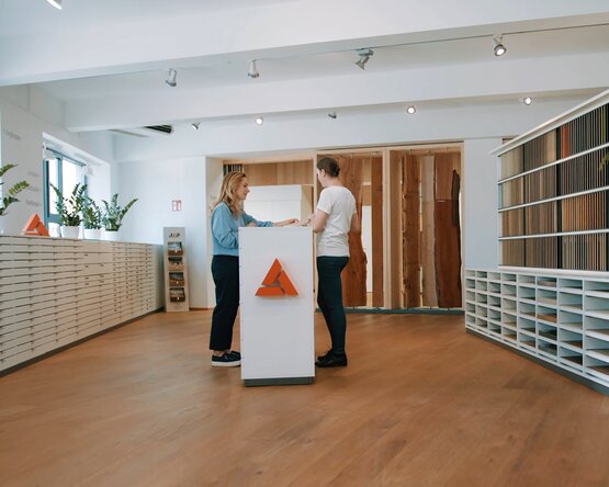 Ein moderner Schauraum mit stilvoller Einrichtung, in dem eine Beratungssituation stattfindet. Der Raum ist hell und einladend gestaltet, mit Mustern und Materialien zur Auswahl. Das Bild vermittelt professionelle Kundenberatung und individuelle Verkaufsunterstützung im persönlichen Gespräch.