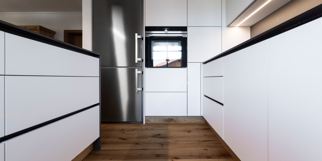 Moderne weiße Küche mit schwarzen Arbeitsflächen, Edelstahlkühlschrank und Holzboden