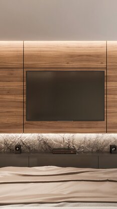 Schlafzimmer mit Holzpaneelwand, integriertem Fernseher und indirekter LED-Beleuchtung hinter dem Bettbereich