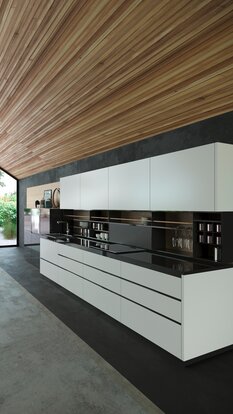 Moderne Küche mit weißen Fronten, schwarzer Rückwand und Decke in Holzoptik mit Griffmulden