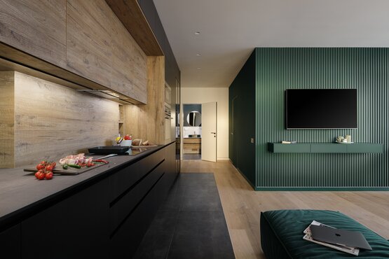 Moderner Wohnraum mit dunkler Küche, Holzoberflächen und grüner Wandgestaltung als Motiv für die Fundermax Interior 2.3 Essential Kollektion