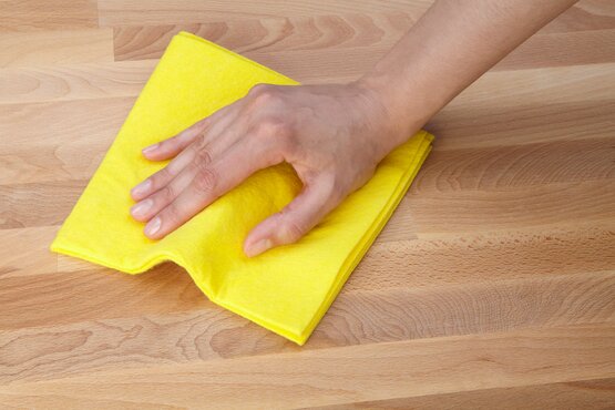 Hand reinigt eine helle Holzoberfläche mit einem gelben Tuch